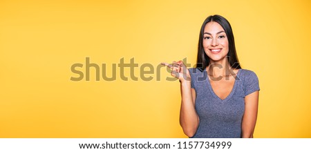 Photo of young excited beautiful happy brunette woman, girl pointing away and smile isolated on yellow background banner