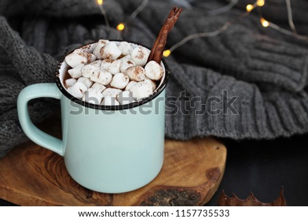 Blue and black enamel cup of hot cocoa with marshmallows and cinnamon bark. Extreme shallow depth of field with focus on drink.