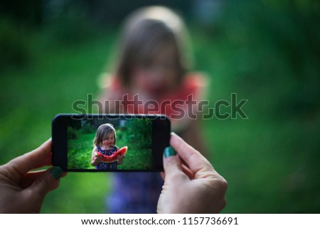 Female hands taking picture of cute little girl eating watermelon
