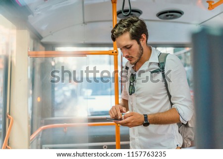 Handsome young man using smartphone in bus.  Handsome man standing in city bus and typing a message on the phone. Businessman commuting to work by bus and working with a smartphone