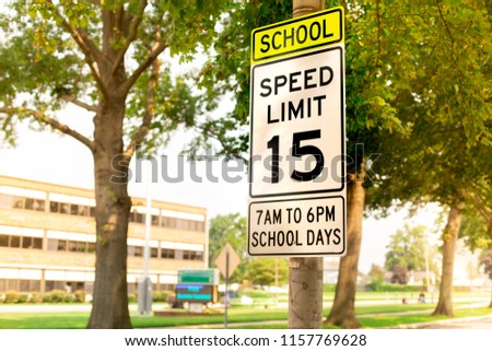 Sign indicating school zone speed limit of 15 miles per hour with school building seen in the background
