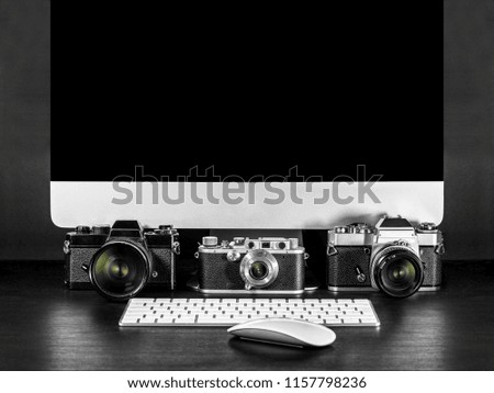 Close up on old film cameras resting on a desktop with a computer