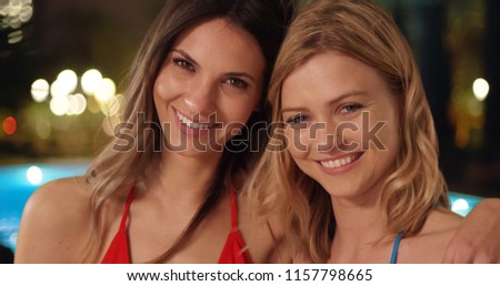 Couple of attractive happy females hanging out together by pool at night