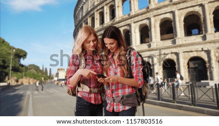 Blonde and brunette traveling in Rome Italy using phone in front of Colosseum