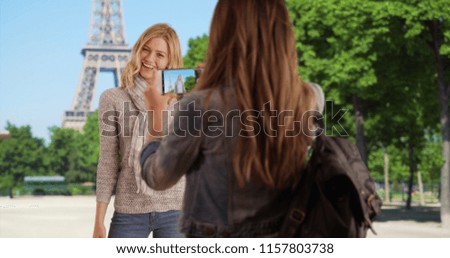 Charming young woman taking picture of friend standing in front of Eiffel Tower