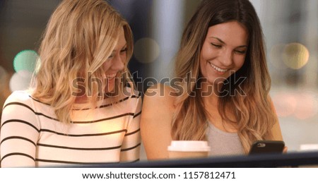 Two lovely girls with smart phone at night in downtown cafe