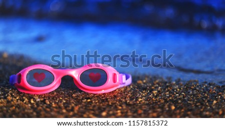 Pink swimming glasses on the sand with the red hearts on the lens. Diving or swimming equipment of the kids. Conceptual picture of the summer vacation, kids drowning or end of the recreation season.