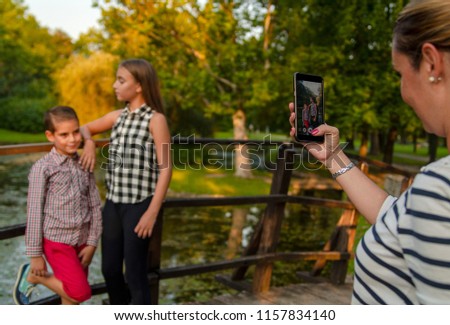 Woman take a picture of kids with cell phone.Little girl and boy posing for photography in beautiful landscape.Tourist take a photo with smart phone