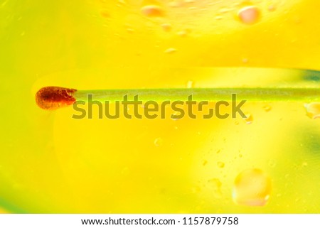 Wooden matchstick with red tip floating on surface of a mixture of oil and water.  