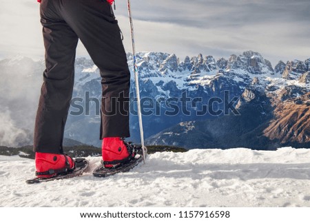 Tall sportsman in warm clothes in snowshoes with trekking poles. Walk in the snow in the mountains.