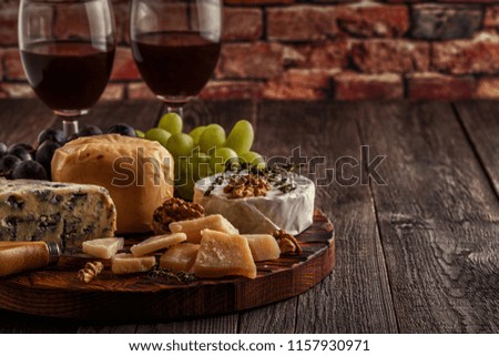 Cheese, nuts, grapes and red wine on wooden background, selective focus.