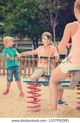 Positive american children are teetering on the swing in the playground.
