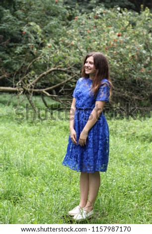 pretty shy girl posing in blue dress in the park, smiling and enjoying good weather