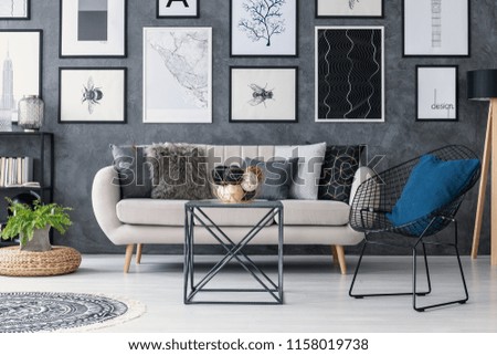 Plant on pouf next to sofa in grey living room interior with table, armchair and posters. Real photo Royalty-Free Stock Photo #1158019738