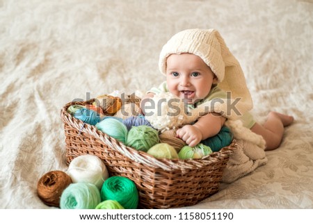 A cute baby lies on a basket with tangles of knitting threads. Hendmeid of multi-colored threads
