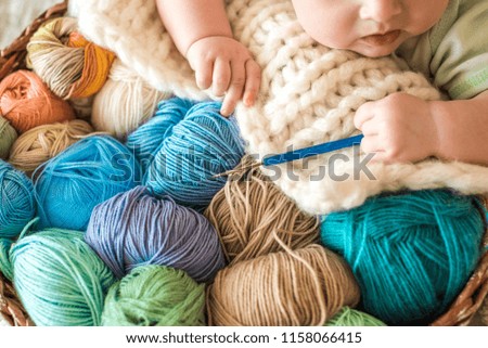 A cute baby lies on a basket with tangles of knitting threads. Hendmeid of multi-colored threads. Children's hands