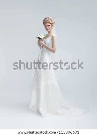 full length picture of lovely young woman in bridal gown with flowers posing over gray background