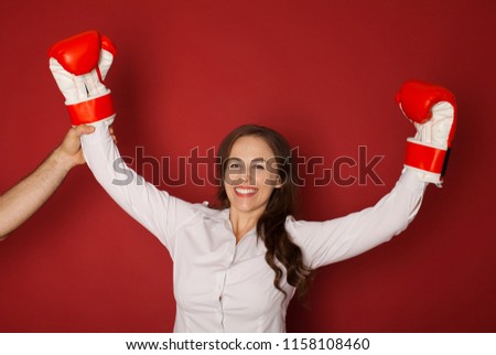 Winning business woman celebrating wearing boxing gloves and business suit. Winner and business success concept photo of young businesswoman isolated on red background.