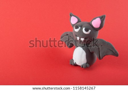 Halloween. Grey bat made of modelling dough staying on red background. Copy space for text