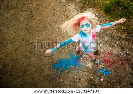 bright blonde girl smiling, her face and hands in colors Holi in blue and pink