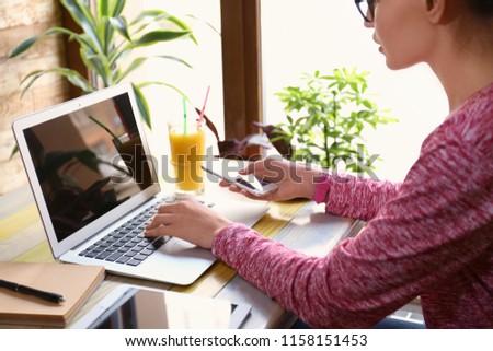 Young freelancer with mobile phone and laptop working in cafe