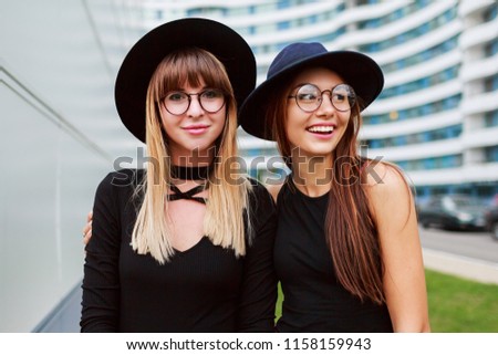 Close up portrait of two fashionable women embarrassing and walking together outdoor. Wearing black  outfit. Wound glasses. Friendship concept.