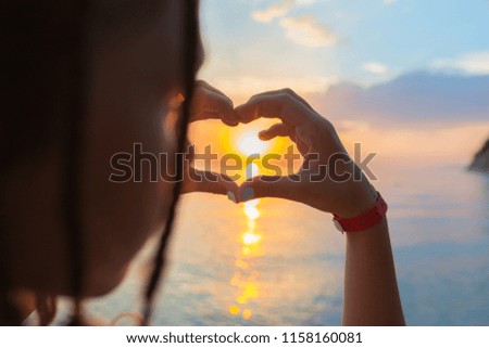 A young girl making heart symbol with her hands at sunset (lens focus on hands)
