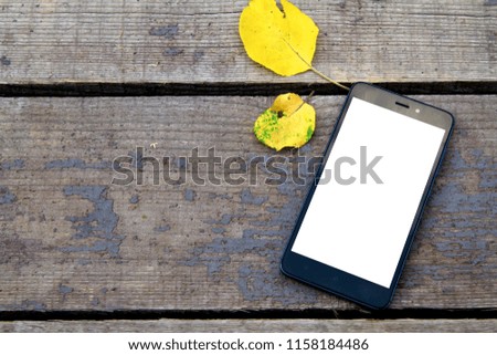 mobile phone on a wooden old autumn background, near the yellow autumn leaves.