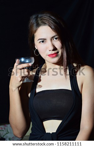 Beautiful Asian Hispanic middle age woman wearing black sleeveless holding wine glass. Dark Background, Close up