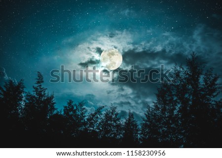 Beautiful night sky with many stars and full moon behind partial cloudy above silhouettes of trees. Serenity nature background. The moon taken with my camera.