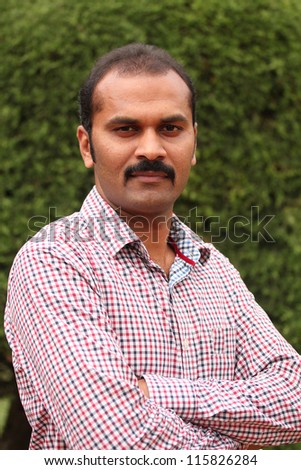 Close-up photo of confident, composed asian/indian man. The business man is wearing a formal shirt & the picture is shot in natural settings