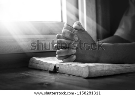 Close up hands of young man praying and reading holy bible, christian black white concept