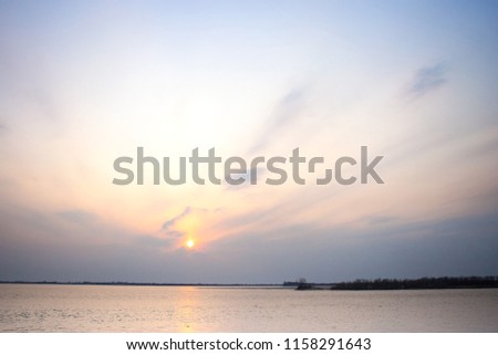 Colorful, amazing sunset on the river with beautiful clouds in the sky, trees, reflections in the water, waves and ripples. Amur. Far East. Khabarovsk. Russia