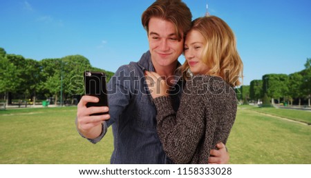 Newly engaged couple taking a selfie in front of the Eiffel Tower smiling