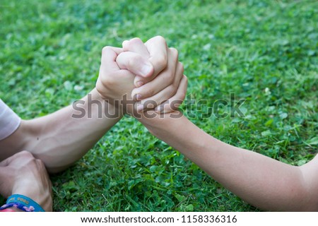 Two clasped hands engaged in an arm wrestle on green lawn