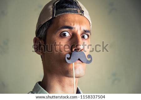 head shot of a man wearing a fake paper mustache looking at the camera Royalty-Free Stock Photo #1158337504