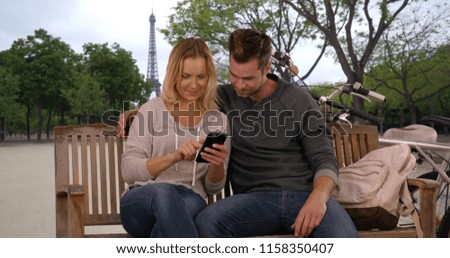 Happy young couple on vacation in Paris looking at selfies with mobile phone