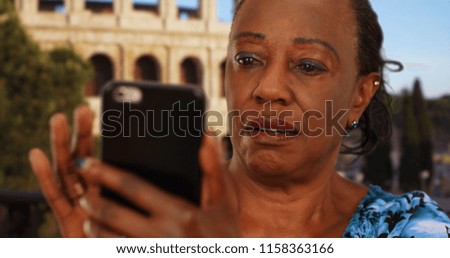 Elderly black woman looks at pictures of grandchildren on smartphone in Rome