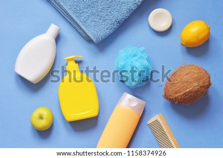 White shampoo bottle, yellow liquid soap package, sponge, hair balm, soap bar, wooden comb, terry towel and fruits. Flat lay photography natural organic bath products. Toiletries kit