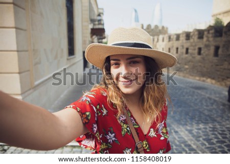 Pretty tourist girl, young woman, taking selfie, self-portrait, in street of Baku old town. Baku, Azerbaijan. 