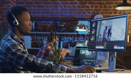 Side view of black man in headphones working on computer and editing video with color correction