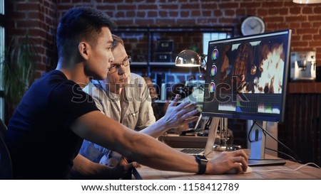 Side view of casual man and producer working on computer and editing video with color correction of documentary or commercial video