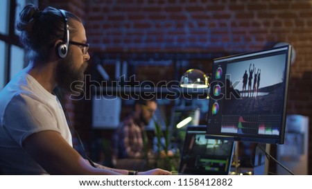 Side view of casual man in headphones working on computer and editing video with color correction Royalty-Free Stock Photo #1158412882