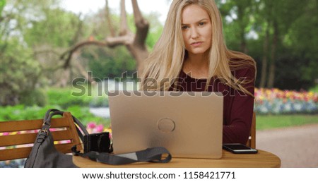 Attractive white blonde girl using laptop near colorful garden stares at camera