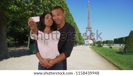 African male and female take photos of themselves near Eiffel Tower in Paris