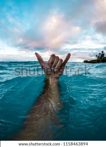 Man's Arm Underwater With Hand Above with Shaka Hand Gesture in Clear Blue Water and Colorful Evening Sky in Tropical Island Paradise Maui Hawaii