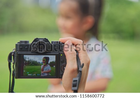 Young cute Asian 4 years old kid postures in the park. Her mother is taking a photo of her. Seen in daylight and focus of camera display.