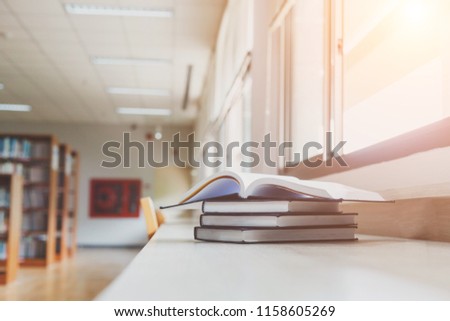 A book on the table in a library. Vintage color filter and Sun light.Blur image of picture library background. Library resources, including vast knowledge. and sun light. Book in library with open tex