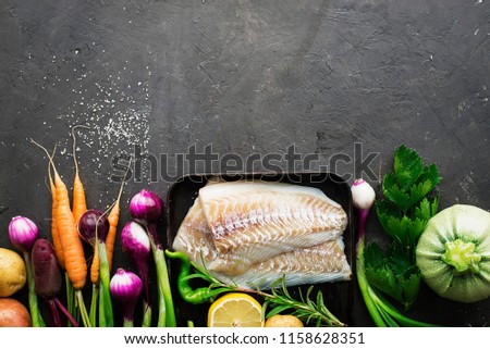 Cod. Fresh sea white raw fish before cooking in a with fresh vegetables: sweet onions, and lemons. Top view. Food concept