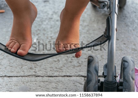 Little girl's feet on a stroller support, close up. 